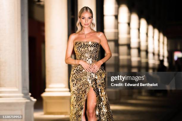 Leonie Hanne wears a necklace, a golden off-shoulder shiny sequin slit long party dress with argyle geometric patterns, during the 78th Venice...