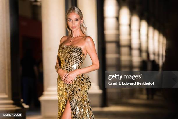 Leonie Hanne wears a necklace, a golden off-shoulder shiny sequin slit long party dress with argyle geometric patterns, during the 78th Venice...