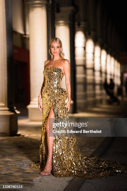 Leonie Hanne wears a necklace, a golden off-shoulder shiny sequin slit long party dress with argyle geometric patterns, during the 78th Venice...