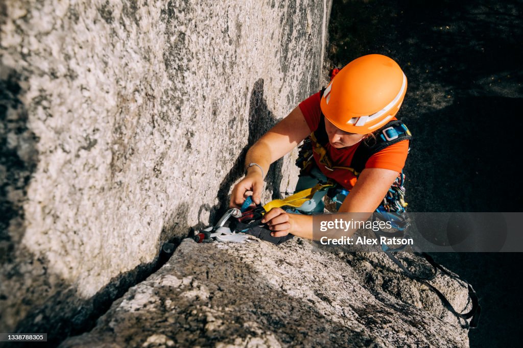 A female rock climber clips into a cam placed in a rock crack high up off the ground