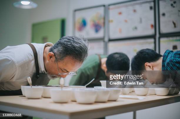 professional asian chinese barista grader performing coffee cupping bending over smelling coffee closely - proeven stockfoto's en -beelden