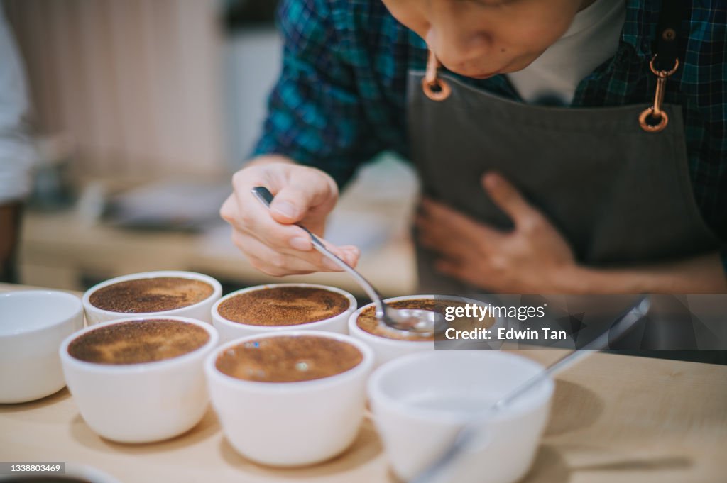 Profesional masculino asiático chino barista calificador que realiza catas de café inclinándose sobre el café que huele de cerca