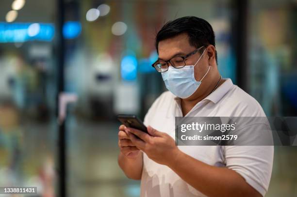 portrait of asian man with face protective mask at the office using smartphone - surgical mask man stock pictures, royalty-free photos & images