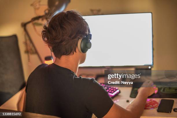 teenager boy playing multiplayer video game on computer wearing headphones - staring at screen stock pictures, royalty-free photos & images