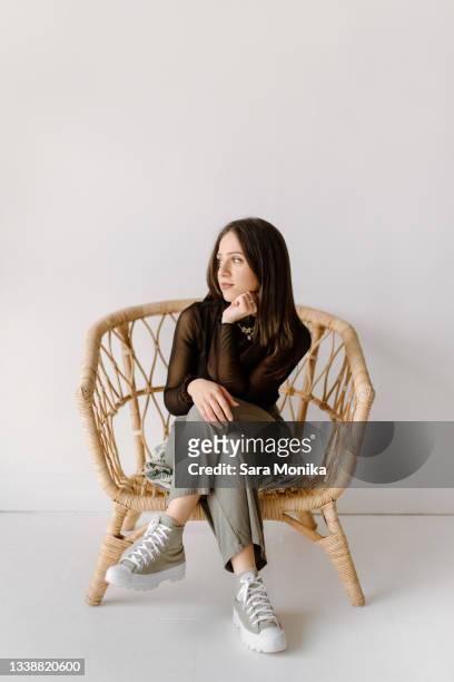 studio shot of young woman sitting in wicker chair - legs crossed at knee stock pictures, royalty-free photos & images
