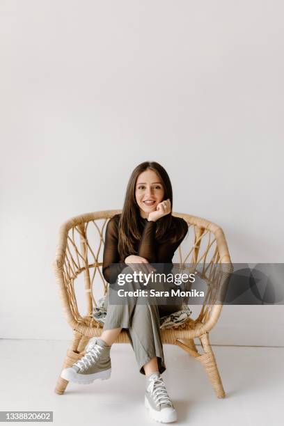 studio shot of young woman sitting in wicker chair - sitting in a chair stockfoto's en -beelden