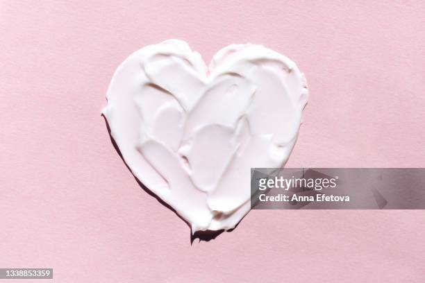 textured smears of white cream applied on pastel pink background in heart shape. body lotion for perfect skin. macrophotography in flat lay style - cosmetique naturel photos et images de collection