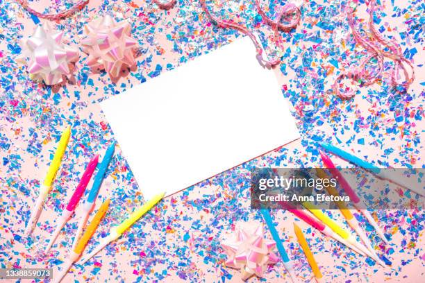 white sheet of paper placed on pink table with birthday candles, string with sequins, holographic bows and many blue and purple foil confetti. holiday backdrop. copy space for your design. flat lay style - birthday template picture stock-fotos und bilder