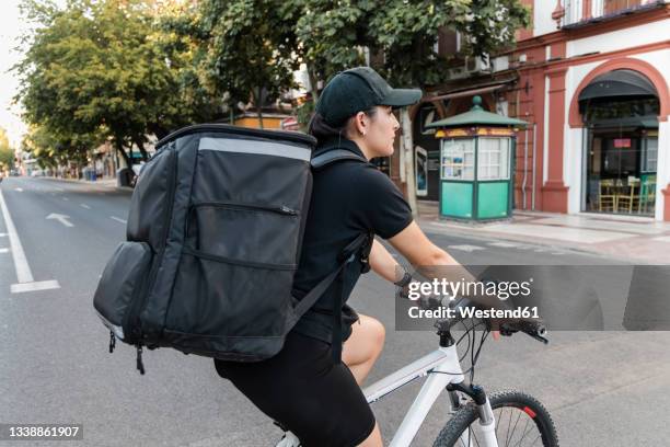 female delivery person with backpack riding cycle on road - bicycle messenger stock pictures, royalty-free photos & images