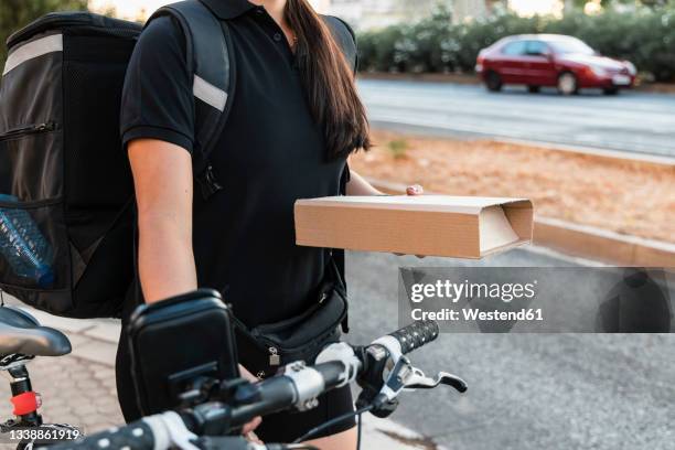 female essential worker holding courier package while wheeling cycle - gig economy stock pictures, royalty-free photos & images