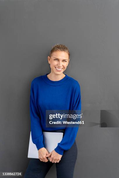 cheerful businesswoman holding laptop while leaning on black background - frau mittleren alters stock-fotos und bilder