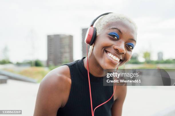happy woman listening music through headphones at park - blå ögonskugga bildbanksfoton och bilder