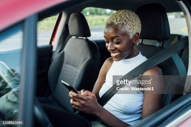 smiling woman using mobile phone while sitting in car - förarsäte bildbanksfoton och bilder