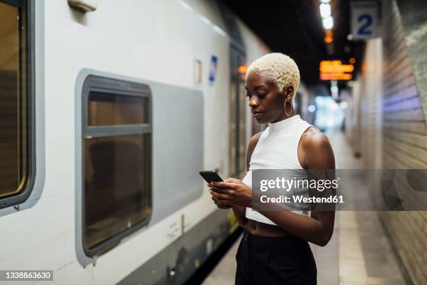 young woman using mobile phone while standing at subway station - black woman short hair stock pictures, royalty-free photos & images