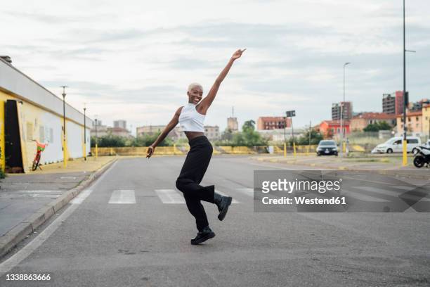 smiling woman with hand raised dancing on street in city - dancer foto e immagini stock