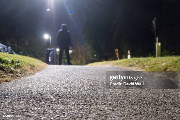 low angle of a mysterious hooded figure standing under a street light, on a summer's night. uk - crime in the uk stock pictures, royalty-free photos & images