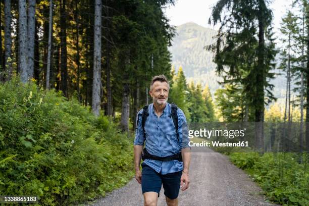 man with backpack walking on road amidst trees - homem 55 anos imagens e fotografias de stock