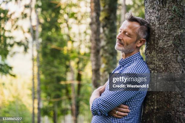 mature man with eyes closed leaning on tree at forest - forest bathing stock pictures, royalty-free photos & images