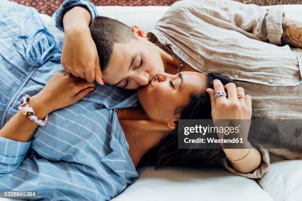 lesbian women kissing while lying together on sofa at home - kissing mouth stock pictures, royalty-free photos & images