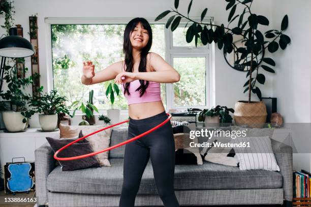 smiling woman exercising with plastic hoop in living room - hoelahoep stockfoto's en -beelden