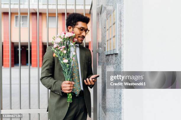 businessman holding bouquet and mobile phone while standing by wall - bouquet de fleurs photos et images de collection