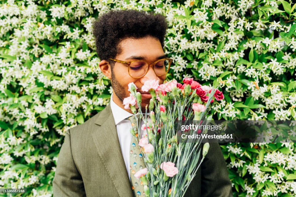 Businessman smelling bouquet in front of flowering plants