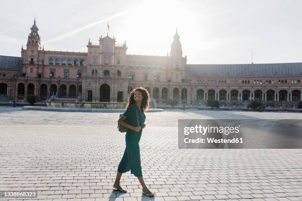 smiling young woman looking away while walking at plaza de espana, seville, spain - seville stock pictures, royalty-free photos & images