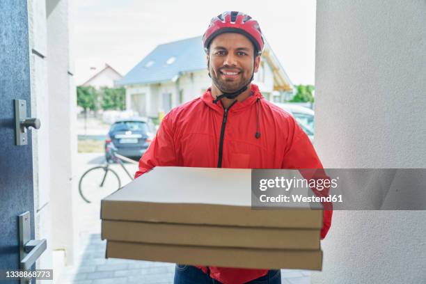 male delivery person holding pizza box while standing at doorway - pizzaschachtel stock-fotos und bilder