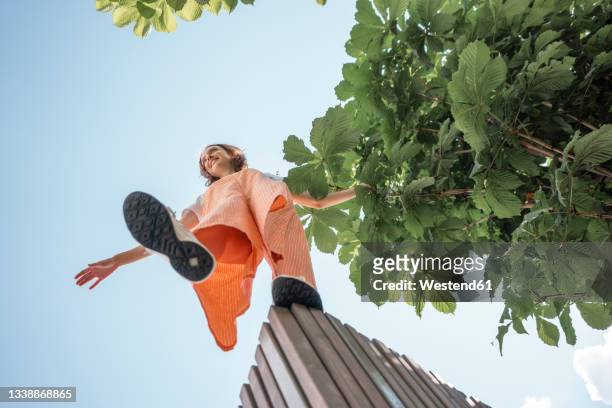 woman with arms outstretched standing on retaining wall - gleichgewicht stock-fotos und bilder