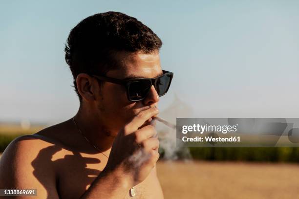 young man with eyeglasses smoking marijuana joint - human joint ストックフォトと画像