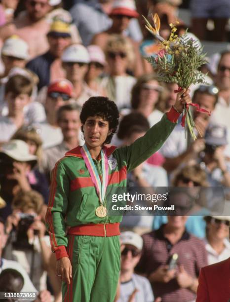 Nawal El Moutawakel of Morocco stands on the podium holding a bouquet of flowers after receiving her gold medal for winning the inaugural Women's 400...