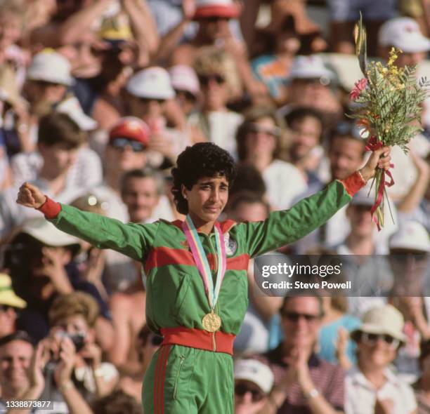 Nawal El Moutawakel of Morocco stands on the podium holding a bouquet of flowers after receiving her gold medal for winning the inaugural Women's 400...