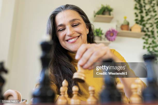 smiling woman playing chess at home - chess stock pictures, royalty-free photos & images