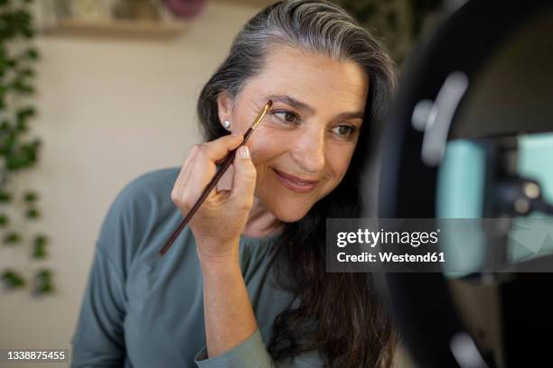 smiling female vlogger brushing eyebrows during tutorial at home - augenbraue stock-fotos und bilder