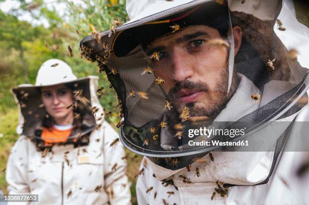 male and female beekeeper with honey bees on protective suit at farm - apicoltura foto e immagini stock