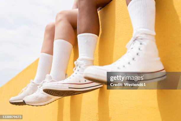 mid adult women wearing white sports shoes on yellow retaining wall - black shoes with white socks stock-fotos und bilder