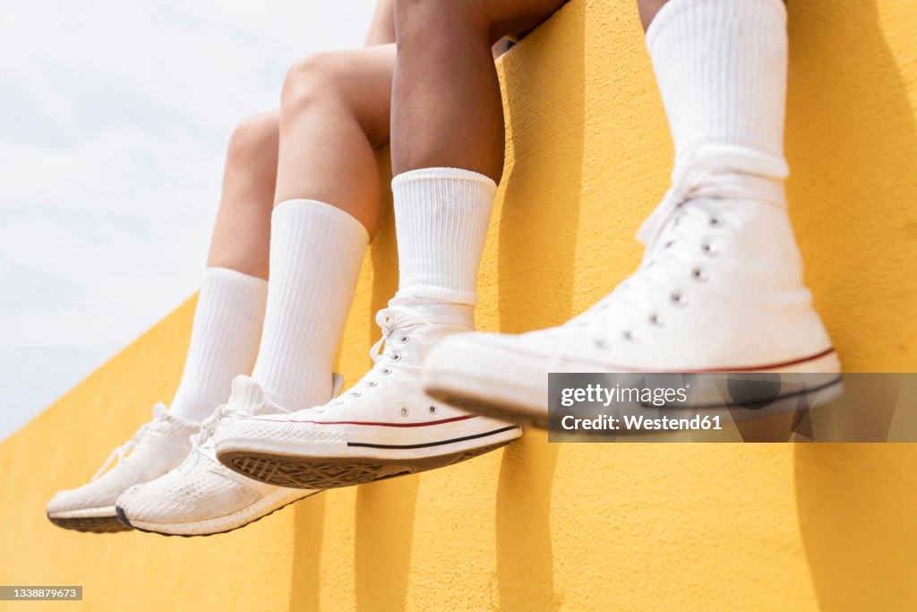 Mid adult women wearing white sports shoes on yellow retaining wall