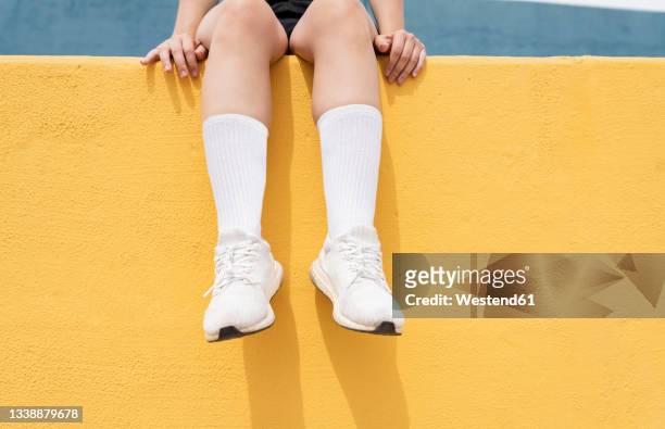 woman wearing white sports shoes sitting on yellow retaining wall - women wearing black stockings stock pictures, royalty-free photos & images