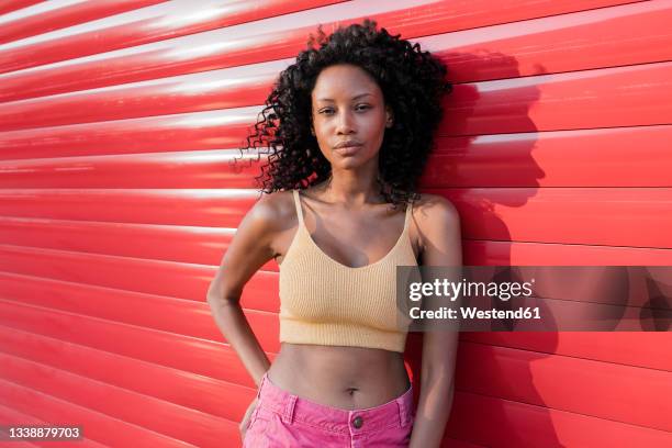 beautiful woman with curly hair leaning on red shutter - cropped tops stock pictures, royalty-free photos & images