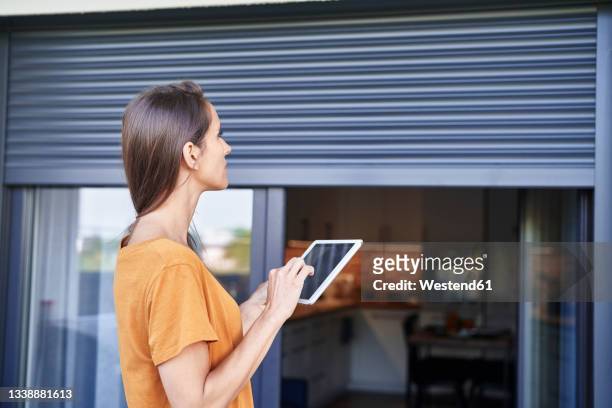 woman controlling blinds through digital tablet - tapparelle foto e immagini stock