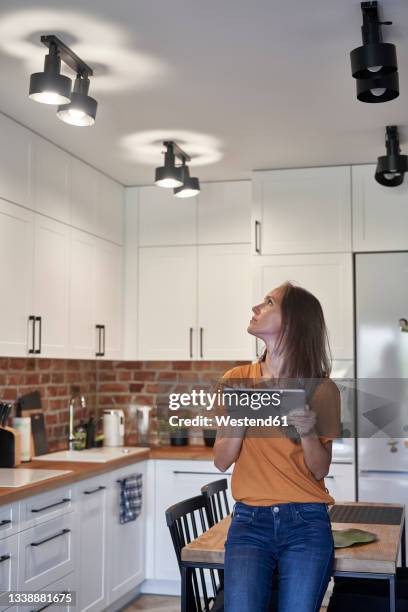 woman controlling lights through digital tablet at home - smart kitchen stock pictures, royalty-free photos & images