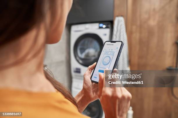 woman operating washing machine through mobile application at home - washing machine stock pictures, royalty-free photos & images