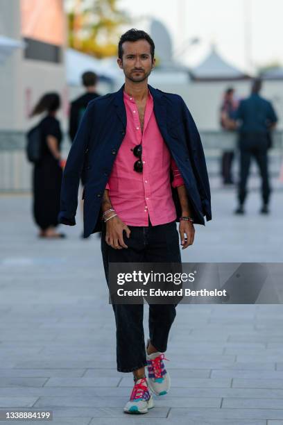 Guest wears a pink fuchsia shirt, black sunglasses, a silver earring, a navy blue blazer jacket, black large pants, a dark green pearls bracelet, a...