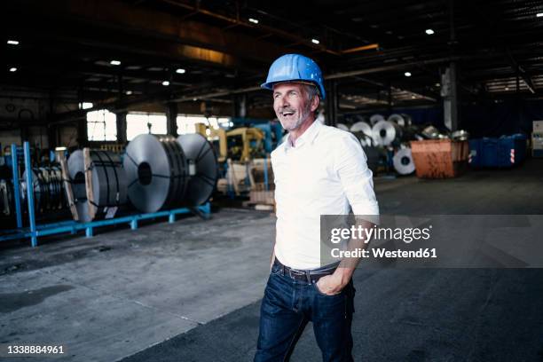 cheerful male engineer with hand in pocket walking in steel mill - metallindustrie stock-fotos und bilder