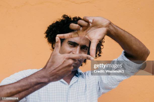 man making finger frame in front of beige wall - antilles occidentales photos et images de collection