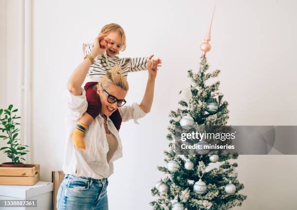 moving in: cheerful mother carrying her daughter on shoulders at home - homeowners decorate their houses for christmas stockfoto's en -beelden