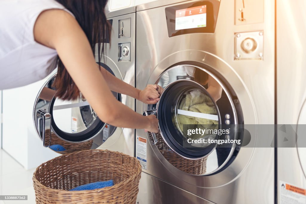 At a laundromat shop with many automatic washing machines, a beautiful woman wearing a mask is doing laundry.