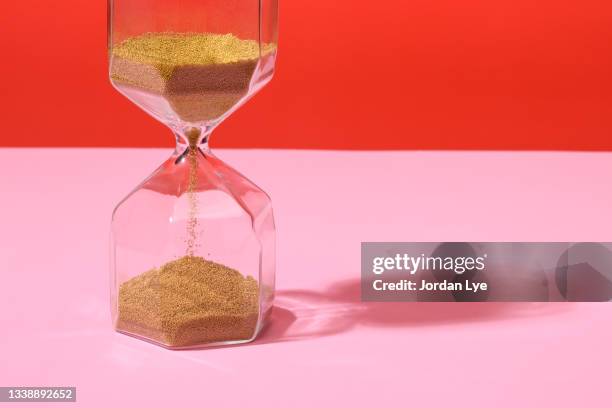 an hourglass on red and pink background - urgenza foto e immagini stock