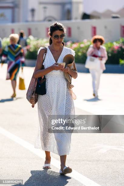 Passerby wears sunglasses, a silver flower pendant earrings, a white cut-out flower print pattern V-neck / sleeveless / belted / flowing midi dress,...