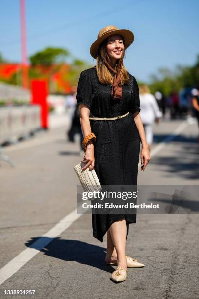 Passerby wears a beige wicker hat with a brown fabric strap, a black shiny leopard print pattern short sleeves / asymmetric midi skirt, a beige...